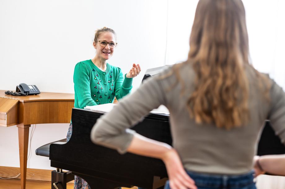 Die Gesangsdozentin Sophie Sauter beim Unterrichten vom Flügel aus. Im Vordergrund ist eine Studentin zu sehen.