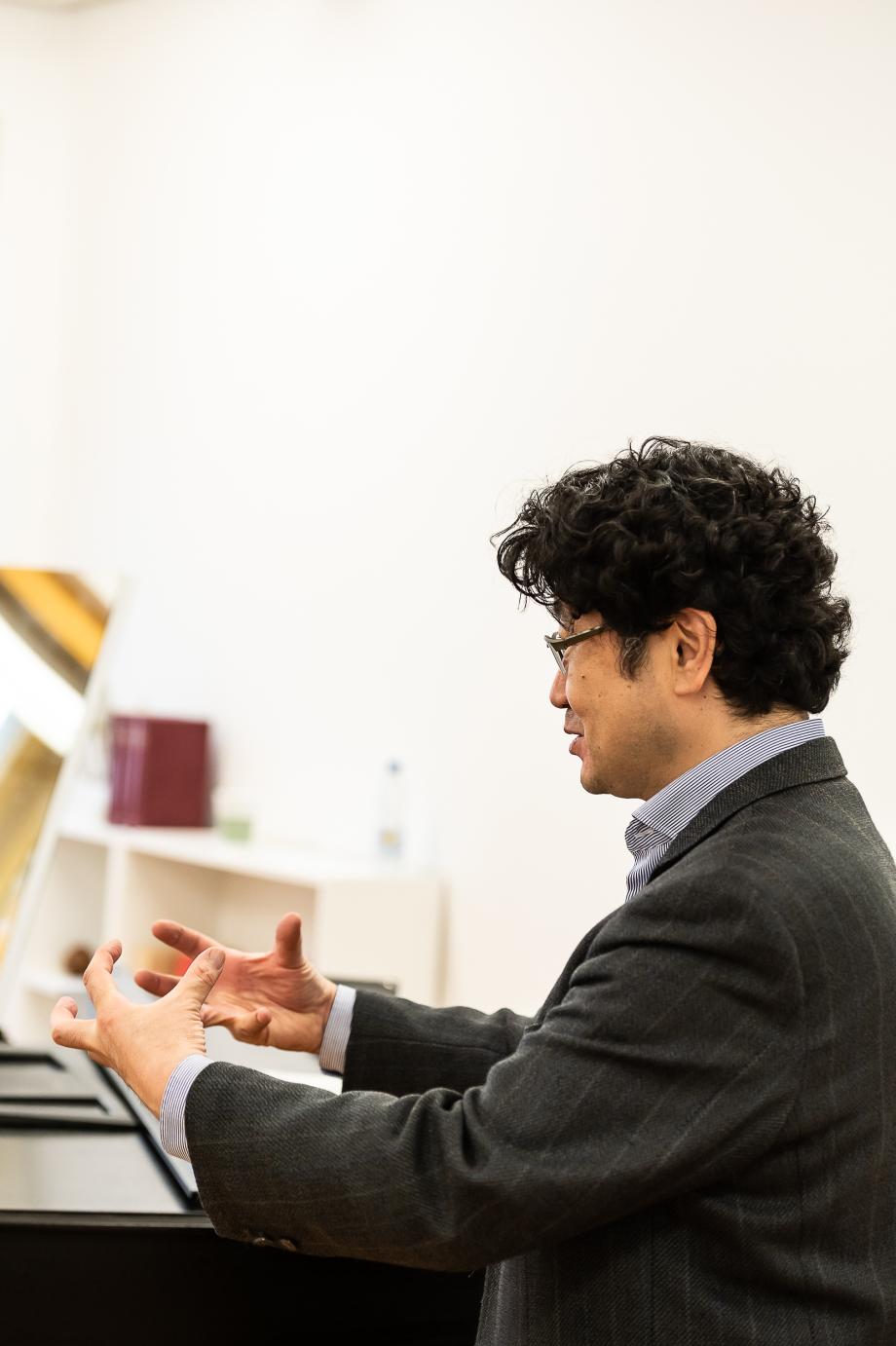 Prof. Teru Yoshihara beim Gesangsunterricht. Er sucht den Blickkontakt zum Gegenüber und formt seine Hände so, als ob sie imaginär einen Ball umfassen würden.