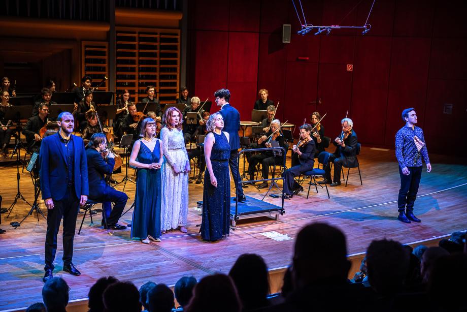 Opernensemble mit Kammerorchester auf dem Podium.