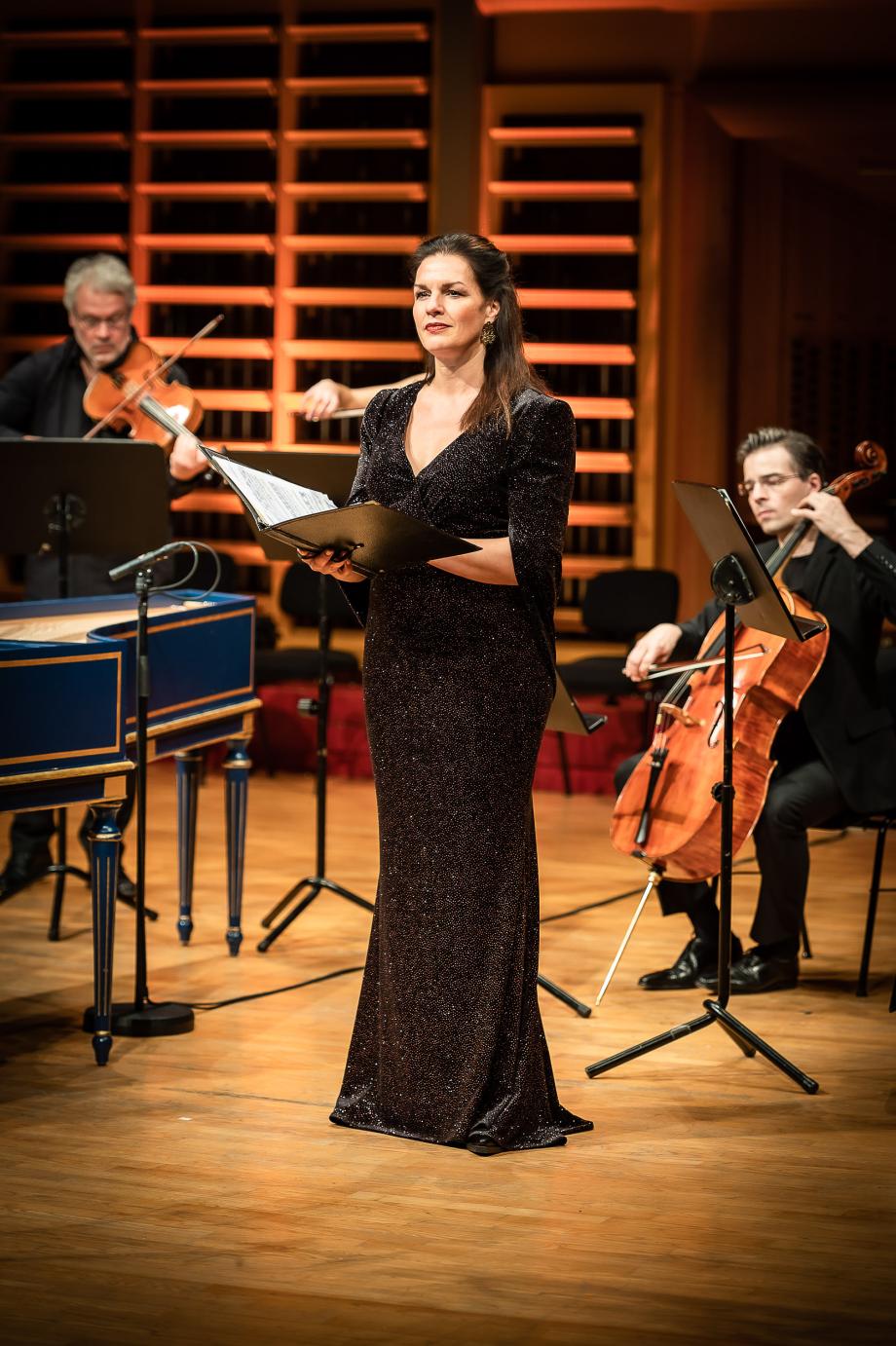 Prof.in Marion Eckstein beim Konzertieren auf dem Podium. Sie trägt ein schwarzes Pailettenkleid. Im Hintergrund musizieren Prof. Stefan Fehlandt und Prof. Tristan Cornut.