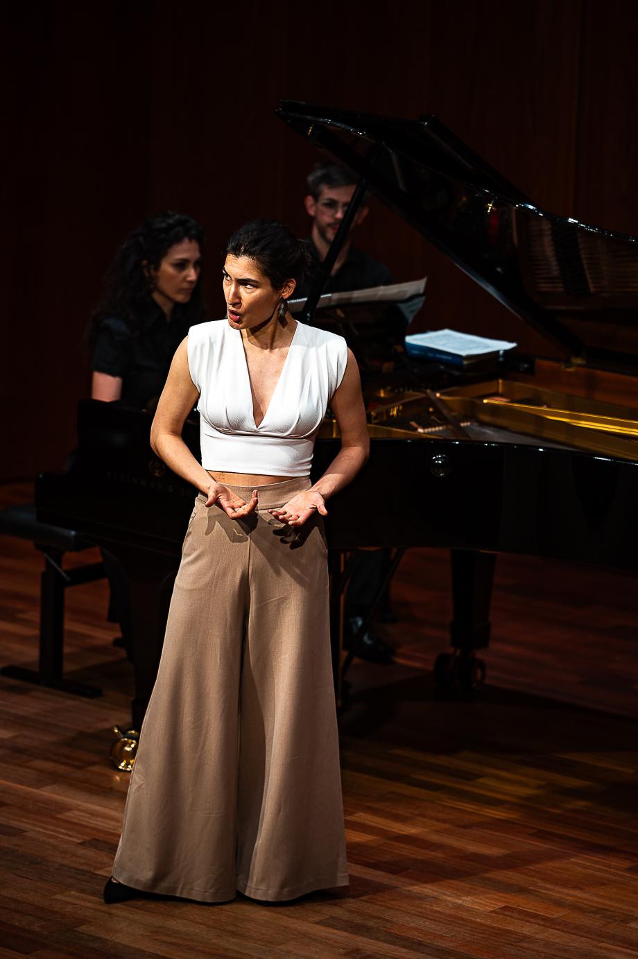 Sängerin blickt mit geneigtem Kopf ins Publikum. Vor ihrem Körper sind die Hände geöffnet.