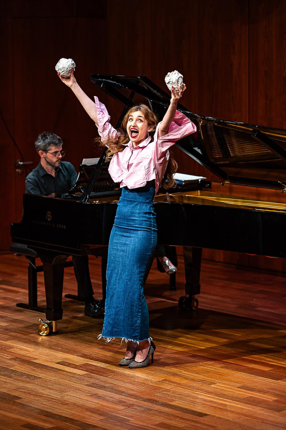 Studentin streckt energisch ihre Arme in die Luft und hält in beiden Händen große Papierkugeln und reißt ihren Mund auf.