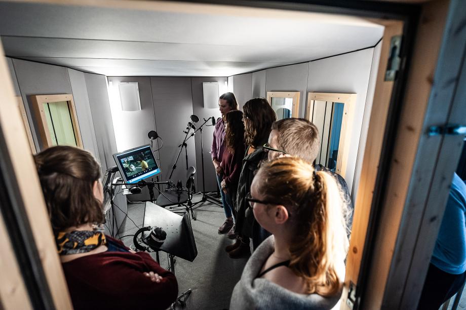 Studierendenensemble in der Sprecherkabine, fokussiert auf einen Monitor.