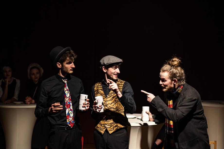 Szene mit drei im Dialog befindlichen Studierenden, die jeweils drei übereinander gestapelte Tassen in einer Hand halten.