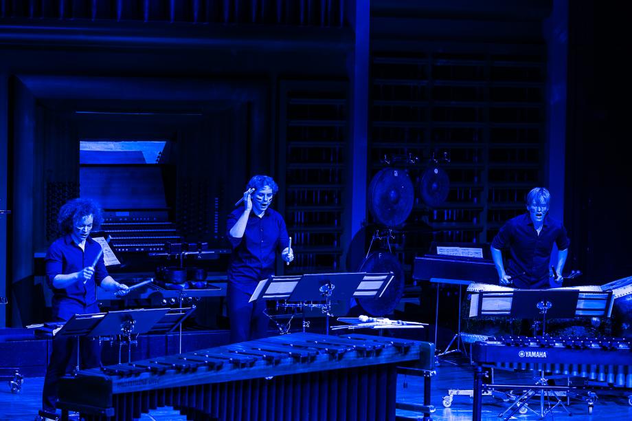 Drei Studierende an Schlaginstrumenten. Das Licht ist blau.