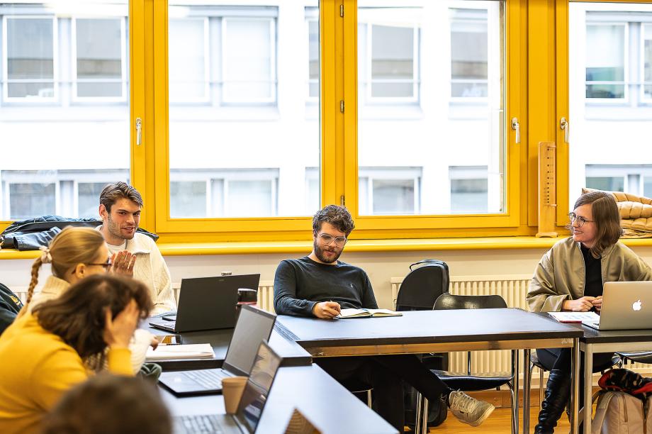 Studierende in einer Seminarsituation im Gespräch mit Prof.in Dr. Karolin Schmitt-Weidmann. Auf den Tischen befinden sich verschiedene Laptops und Tablets.