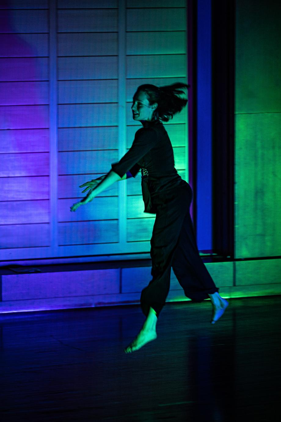 Schwebende Tanbewegung einer Studentin bei der Werkstattbühne von Studierenden der Elementaren Musikpädagogik. Das Orgelprospekt schimmert im Hintergrund in grün-blauen Tönen.