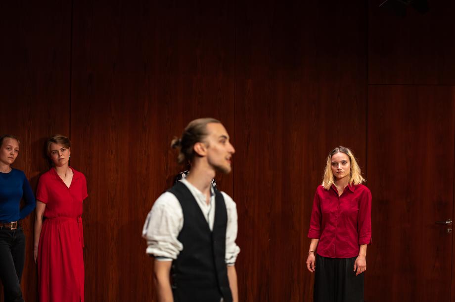 vier Menschen auf Bühne. Mann in Mittelpunkt, drei Frauen schauen ihn an.