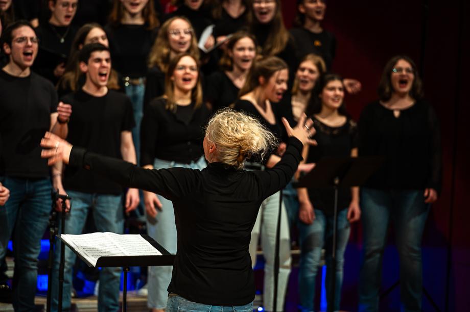 Dirigentin Salomé Tendis steht mit Rücken zum/zur Betrachter*in und dirigiert Chor.