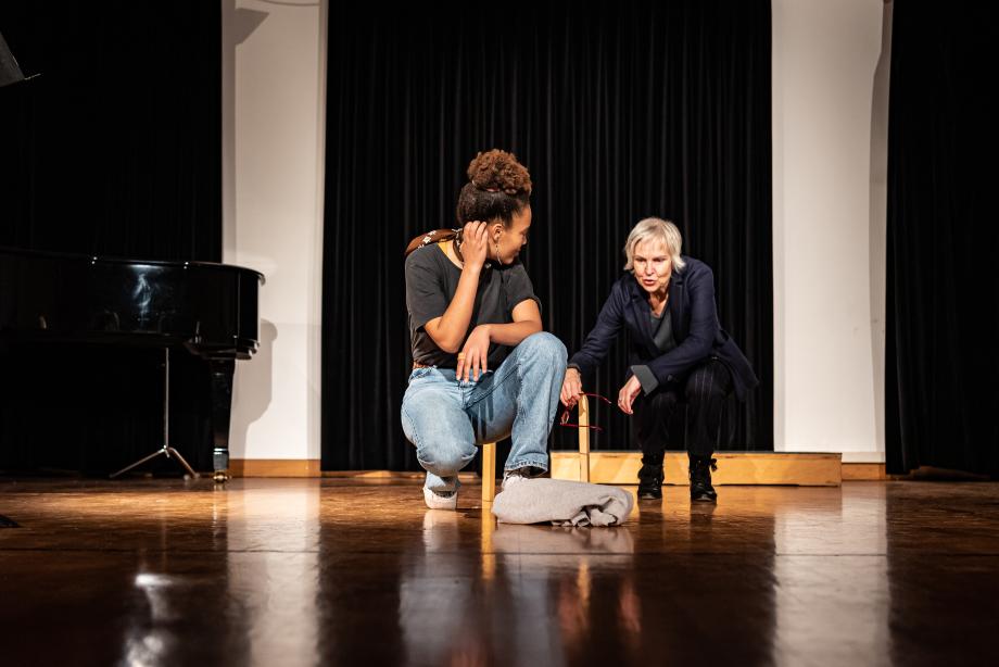 Professorin erklärt Studentin etwas. Beide hocken auf der Bühne.