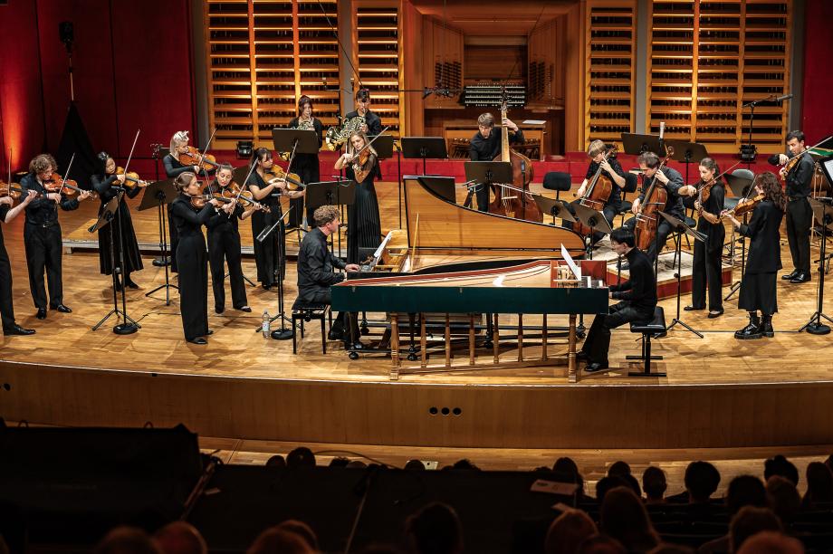 Blick aus dem Zuschauerraum auf die Konzertbühne, wo zwei Cembalisten und das HochschulSinfonieOrchester musizieren.