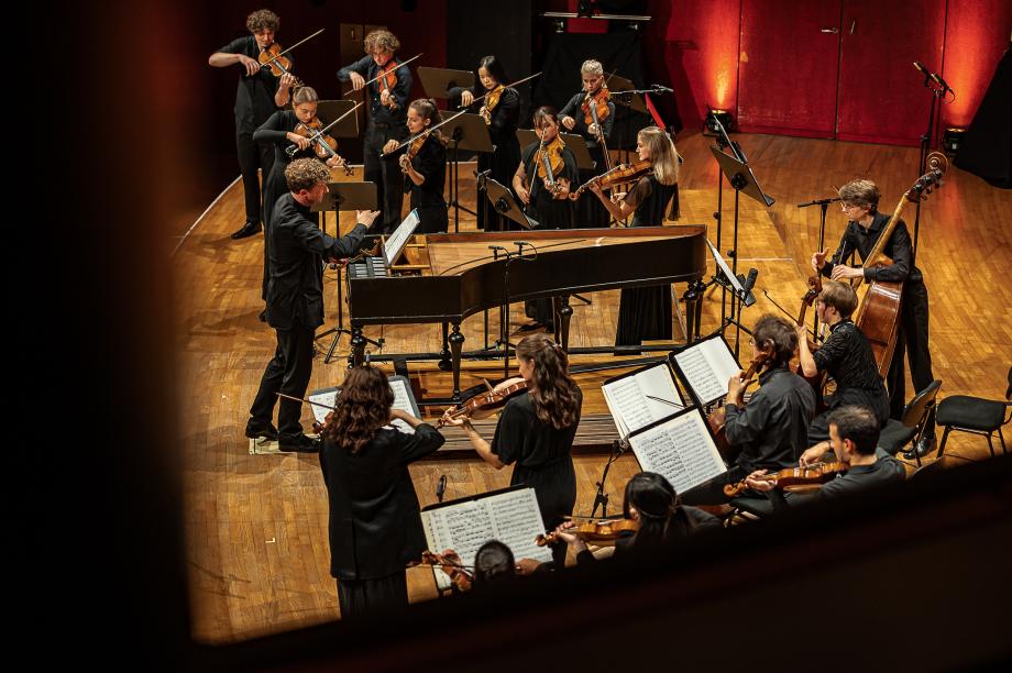 Blick vom Seitenrang auf das Konzertpodium. Jörg Halubek als Mastro al Cembalo mit dem HochschulSinfonieOrchester.