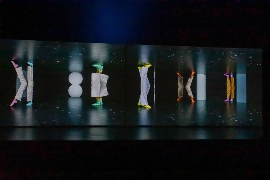 fünf Beine, die sich spiegeln in bunten Socken auf einer schwaren Bühne.