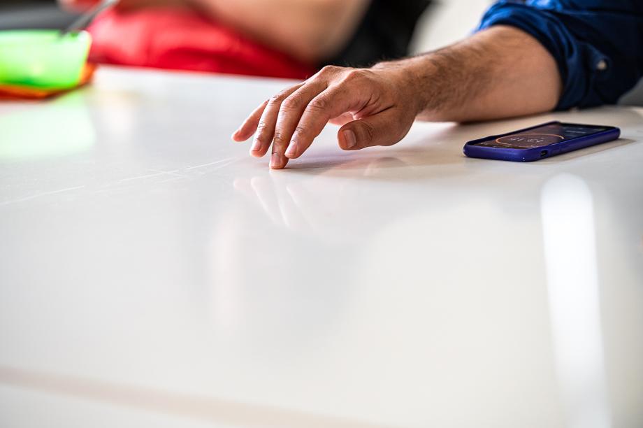 Eine weiße Tischplatte, darauf liegt eine echte Hand. Neben der Hand liegt ein Handy mit einer Stoppuhrfunktion.