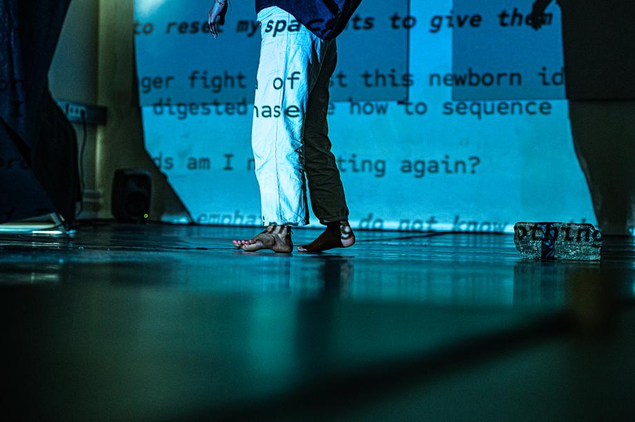 Beine mit nackten Füßen stehen vor Leinwand mit Text.