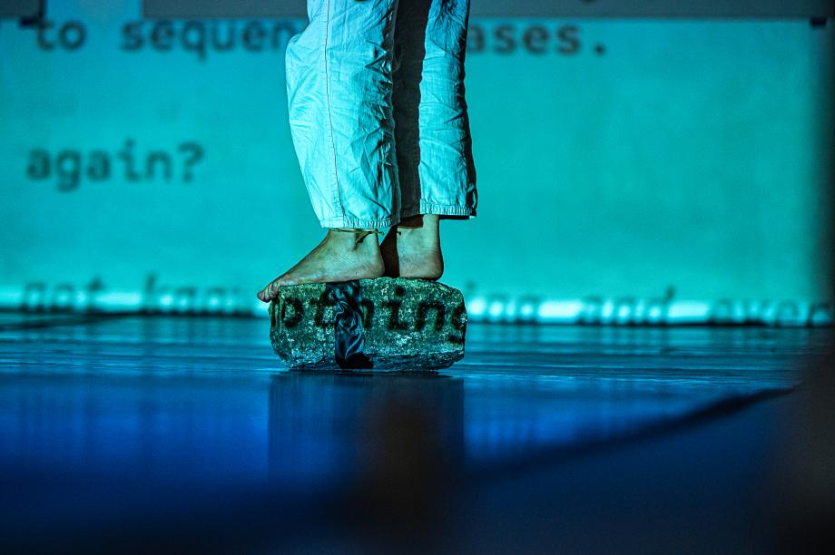 Frau vor Leinwand mit Text steht barfuß auf einem Stein.