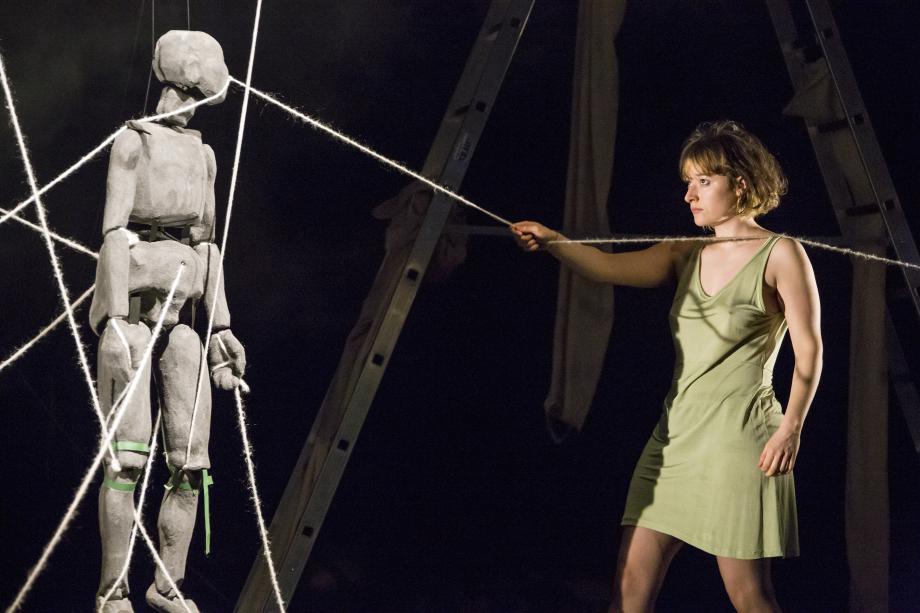 Frau hält eine Schnur in der Hand, die um eine Figur gewickelt ist und schaut diese an.