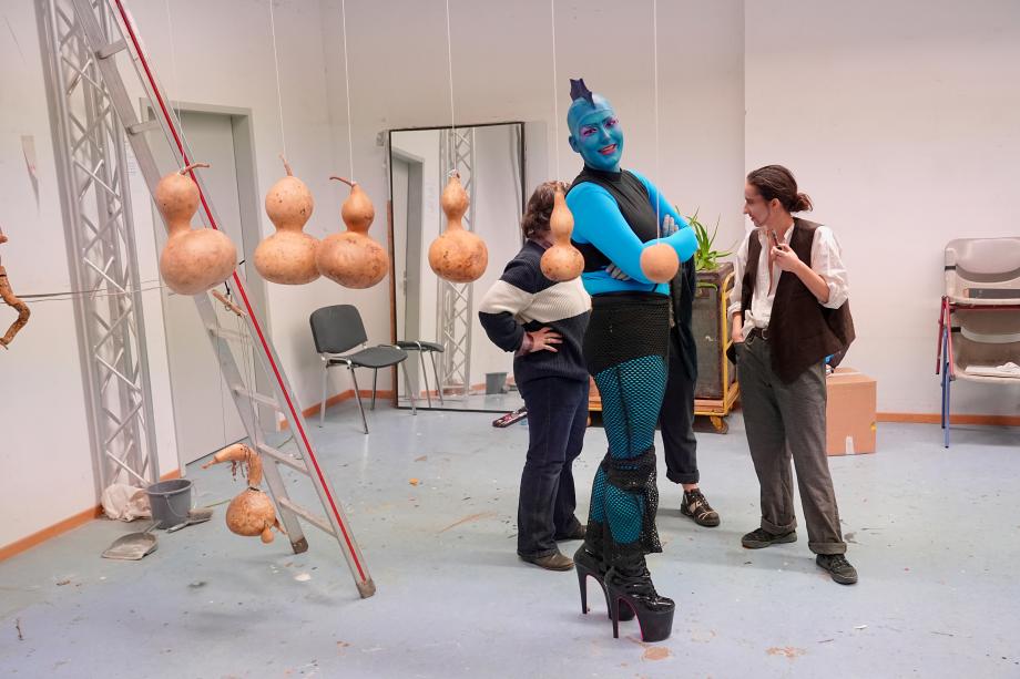 sechs Kürbisse an Schnur an der Decke, Mensch mit blauer Hat und Irokesenschnitt lacht in die Kamera.t