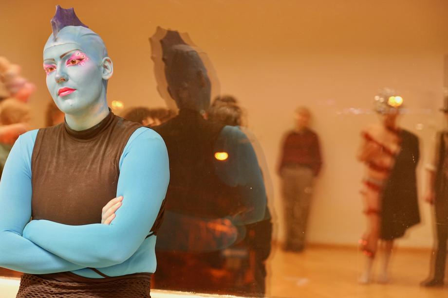 Mensch mit blauer Haut undIrokesenschnitt schaut an Kamera vorbei.