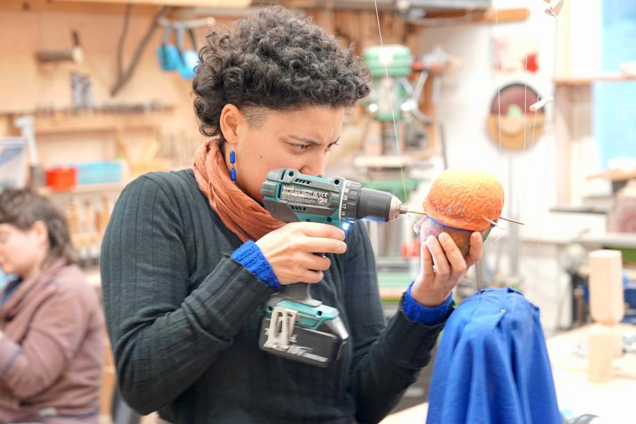 Studentin bohrt mit Bohrmaschine ein Loch in einen Figurenkopf.