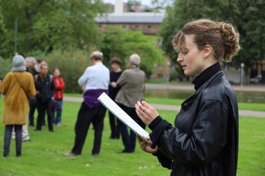 Frau liest von Textbuch auf dem Rasen stehend.