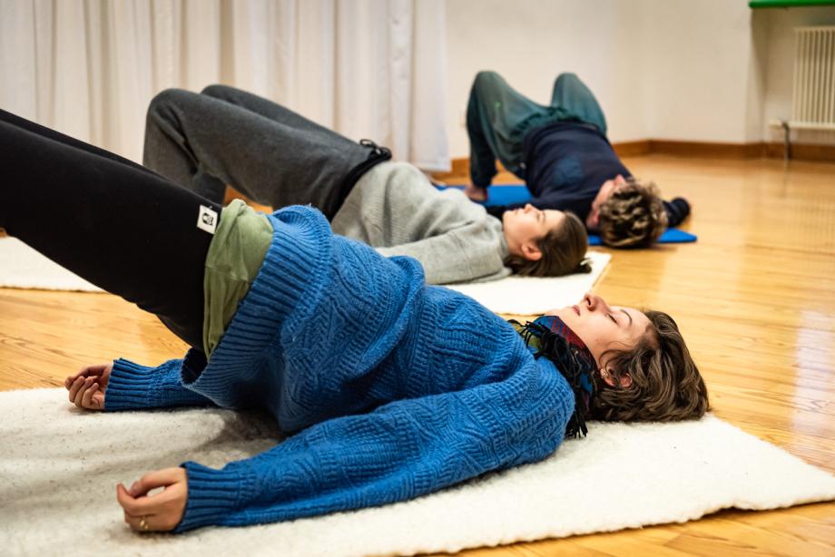 Drei studierende liegen auf Matten am Boden und machen die Brücke.