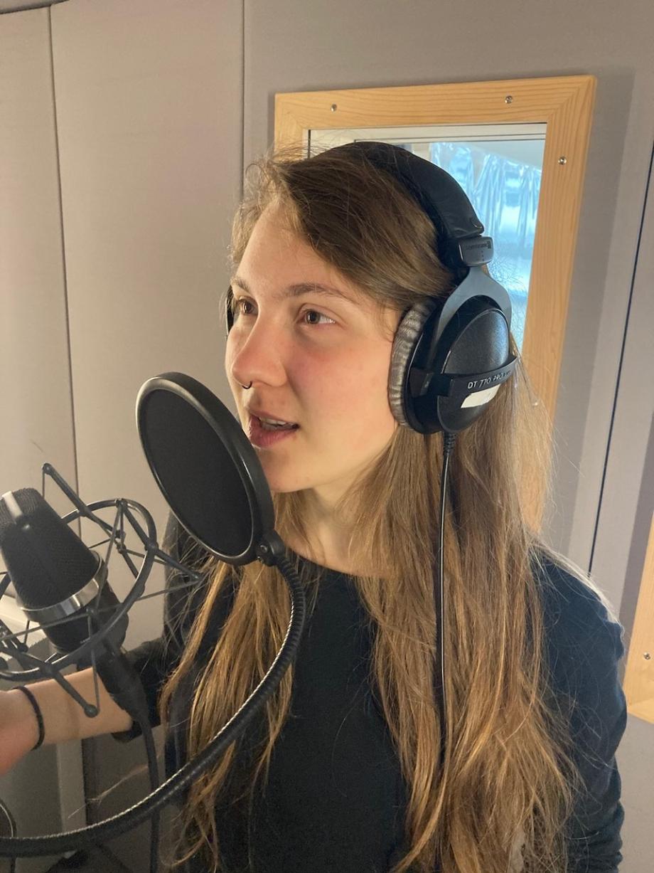 Studentin spricht in Sprechkabine mit Kopfhörern in ein Mikrophon.