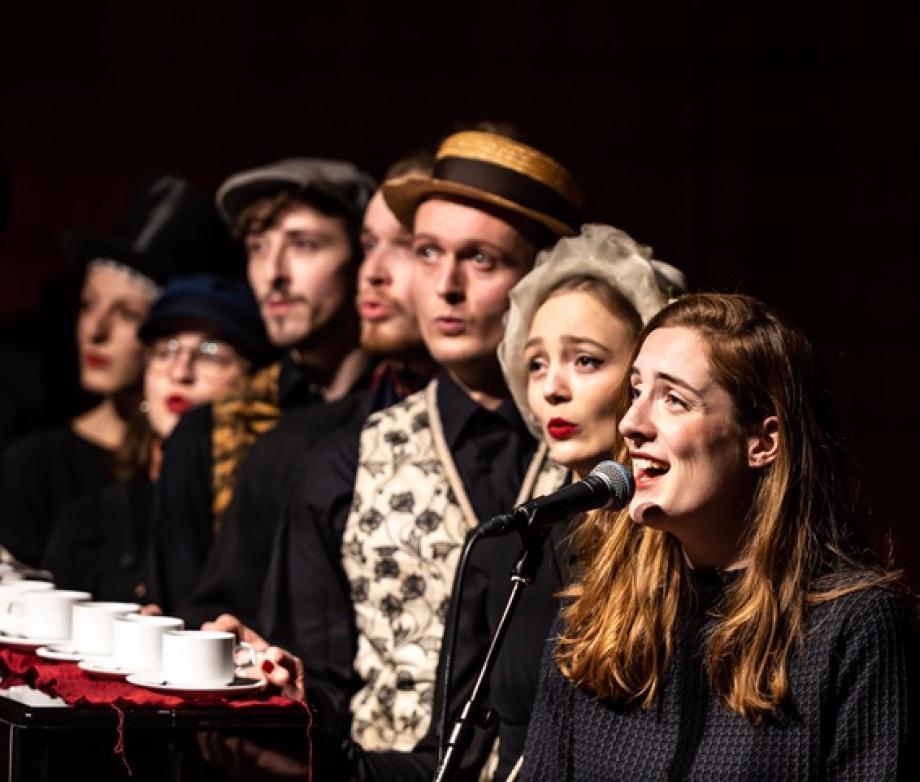 sieben Menschen singen verkleidet auf Bühne.