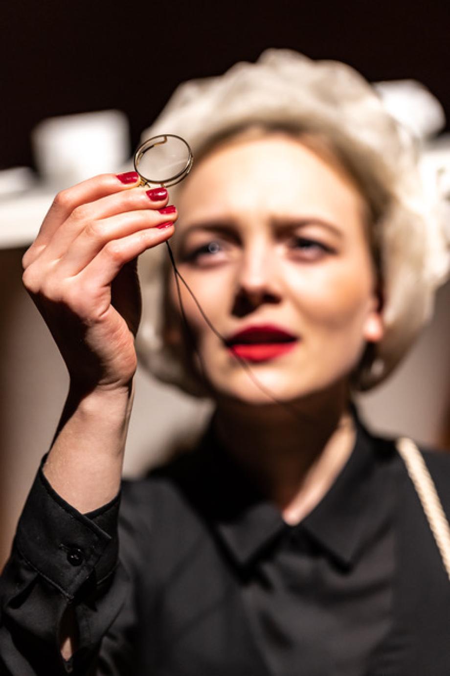 Frau schaut skeptisch mit Abstand durch Monokel