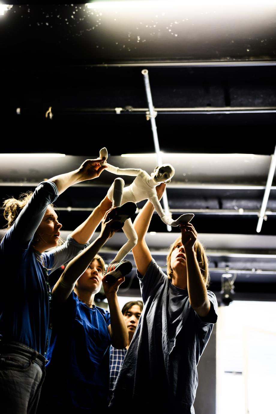 Drei Frauen halten eine kleine Figur über ihren Köpfen und schauen sie an.