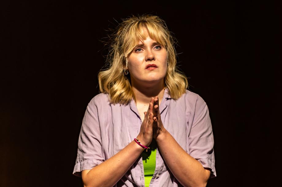 Portraitaufnahme einer Studierenden während des Stücks. Sie hällt ihre Hände aneinander und schaut in die Ferne.