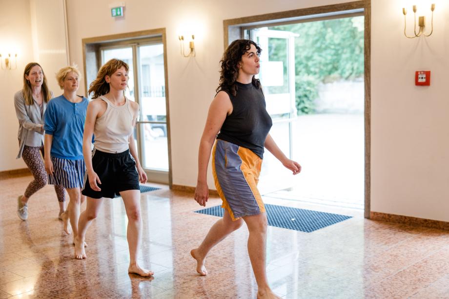 vier Frauen laufen in einer Reihe über einen Steinboden.