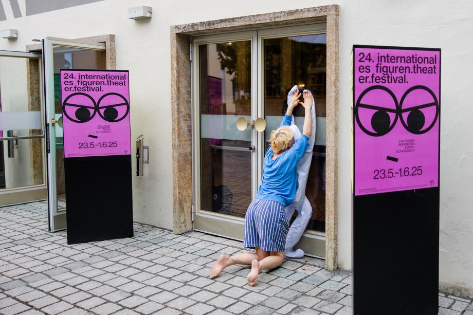 knieende Frau drückt eine Kunststoffhülle in Form einer Figur mit ihrem Körper gegen eine Glastür.