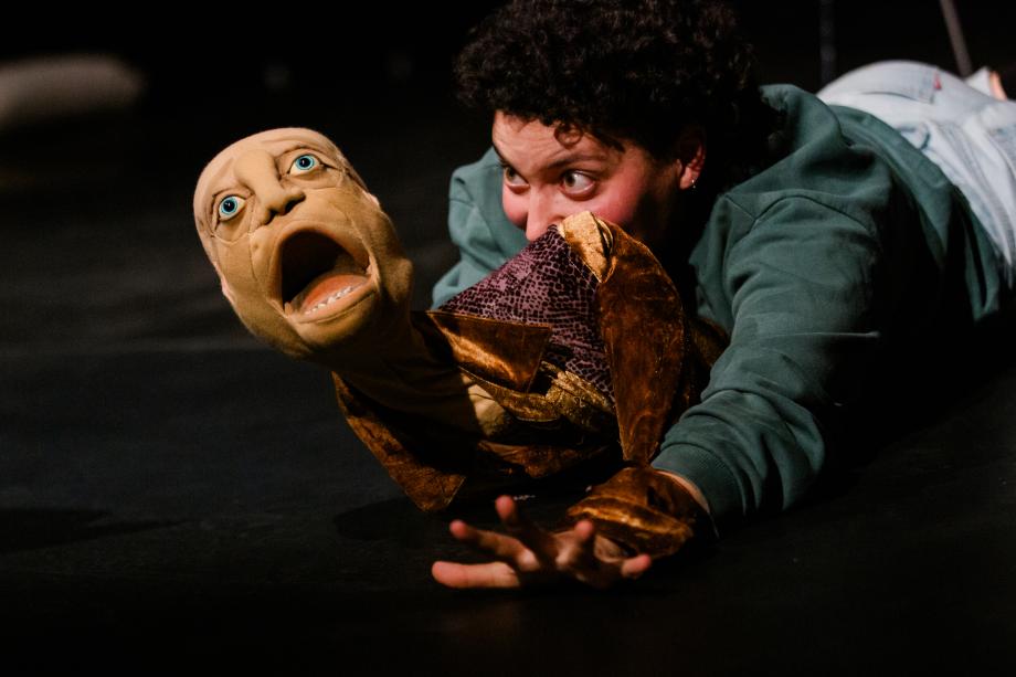 Eine Frau liegt auf dem Bauch und schaut auf einen Figurenkopf, den sie in der Hand hält. Der Kopf hat den Mund aufgerissen.