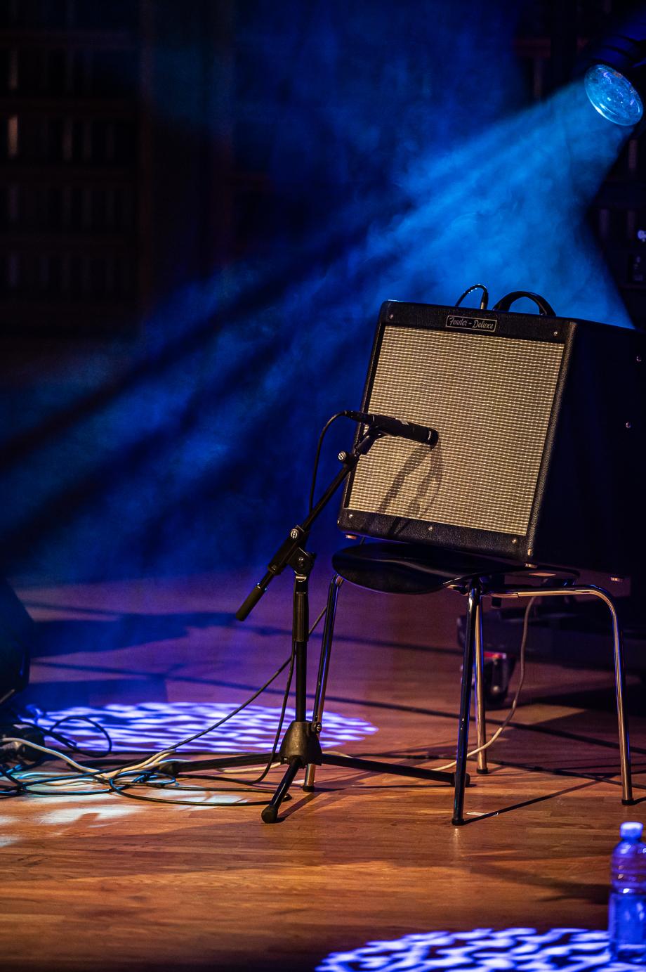 Ein Gitarrenverstärker steht auf einem Stuhl auf einer Bühne im Scheinwerferlicht.