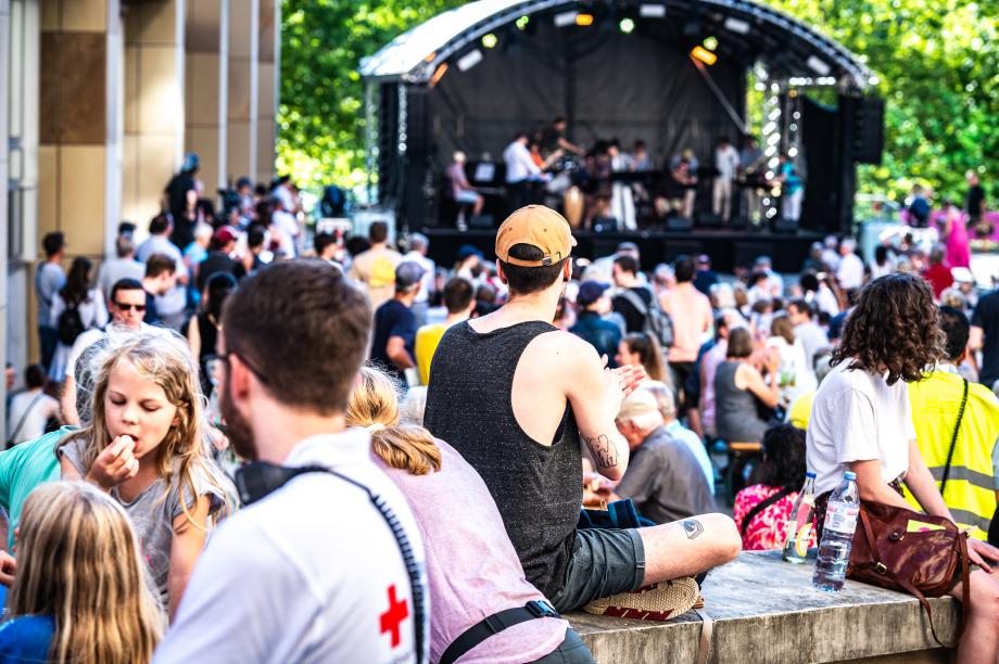 Menschen unterschiedlichen Alters sitzen an Tischen oder stehen auf der Piazza vor der Hochschule. Im Hintergrund auf einer Bühne spielt eine Big Band.