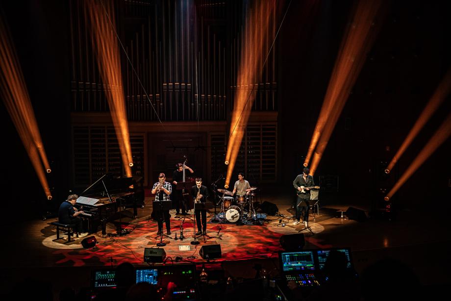 Im Konzertsaal der Hochschule spielt ein Jazz-Sextett. Die Bühne ist farbig beleuchtet.