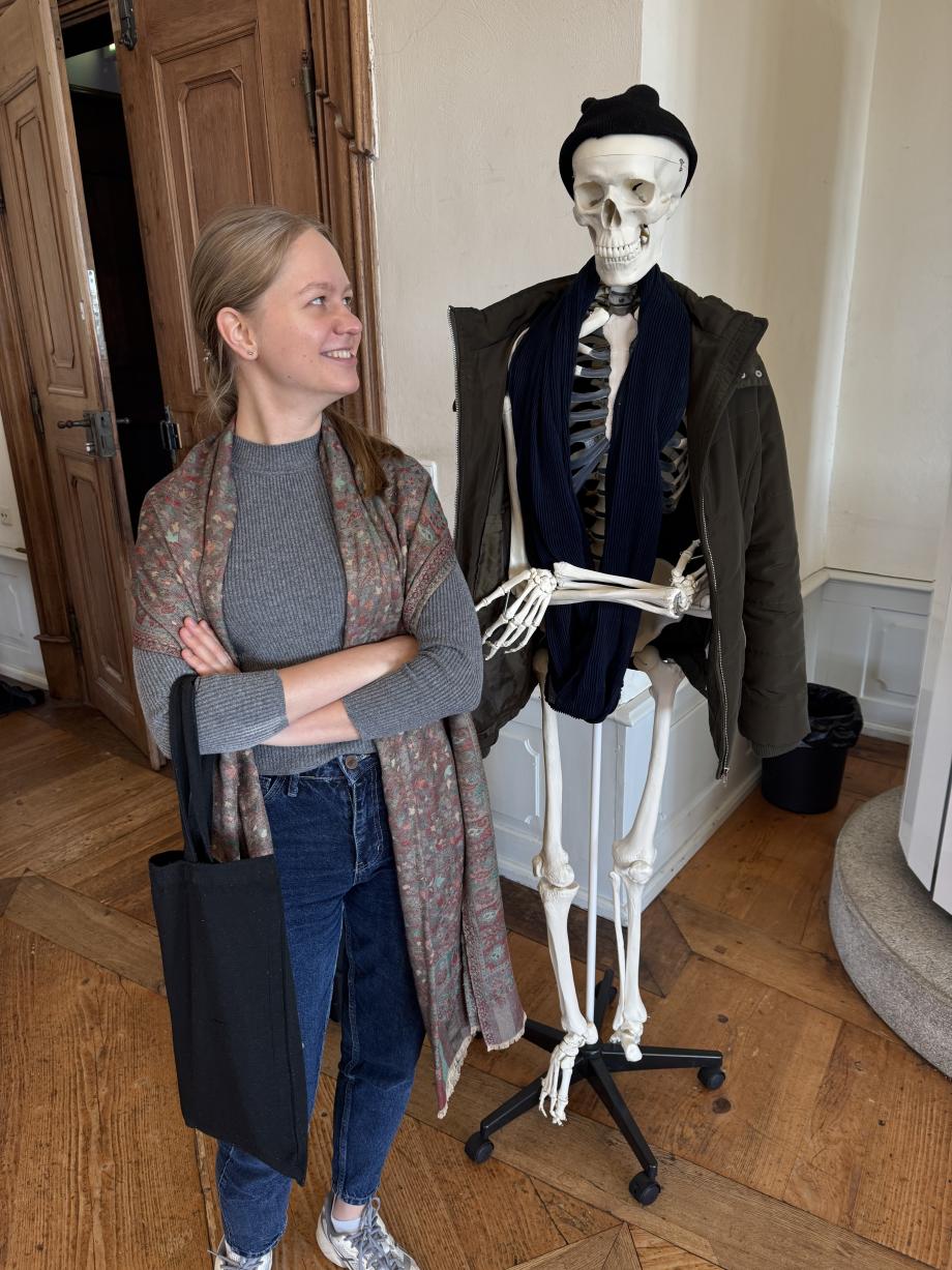 Eine Studentin steht neben einem Skelett, das kostümiert ist.