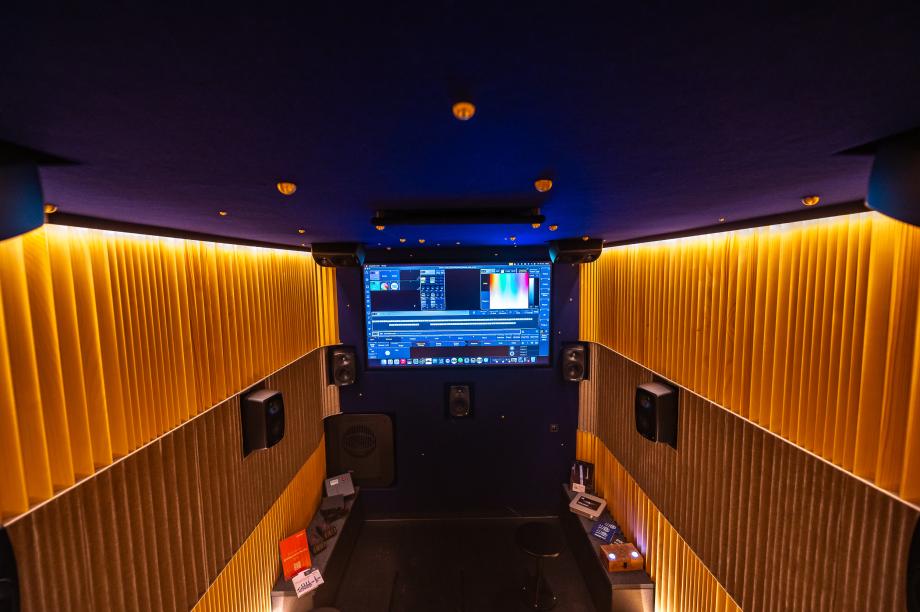 Kleiner Konzertsaal mit gelb beleuchteten, vertikal geriffelten Wänden, schwarzem Boden und großer Leinwand mit Computerbildschirm