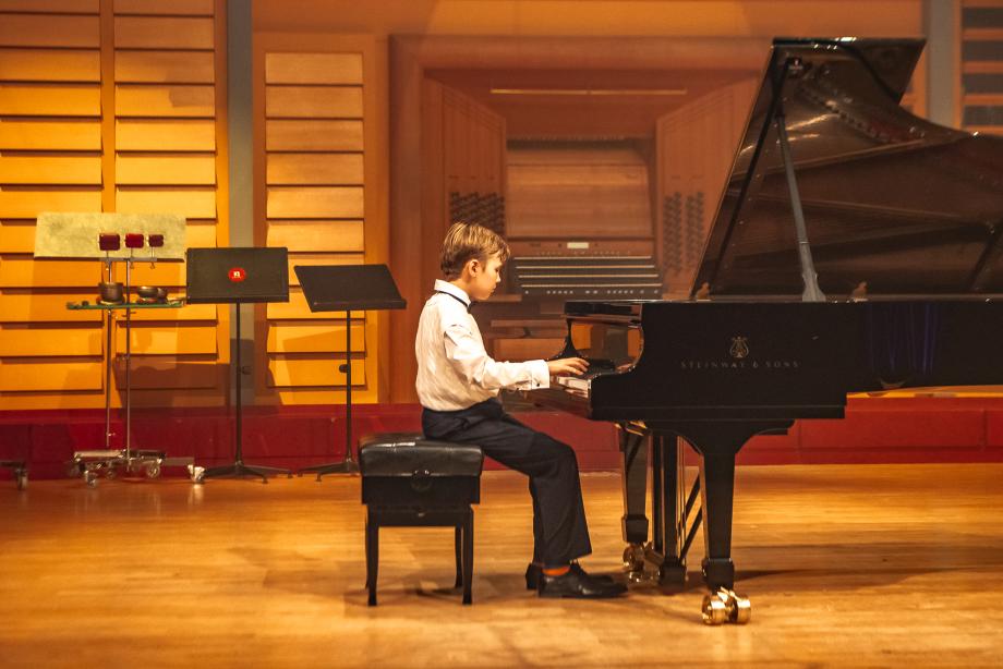 Der junge Musiker Vincent Weingärtner vom Musikgymnasiums Stuttgart sitzt am Konzertflügel gut beleuchtet auf der Bühne im Konzertsaal.