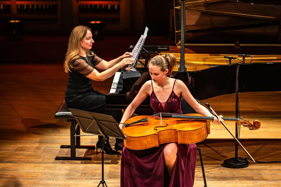 Polina Jakovleva am Flügel, davor sitzt eine Jungstudentin mit einem liegenden Cello auf ihrem Schoß.
