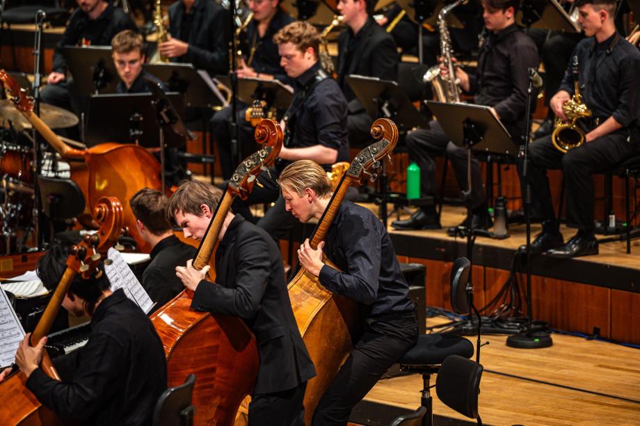 Blick von der Seite auf die agierende Kontrabassgrupee des Hochschulsinfonieorchesters. Im Hintergrund ist die Big Band zu sehen.