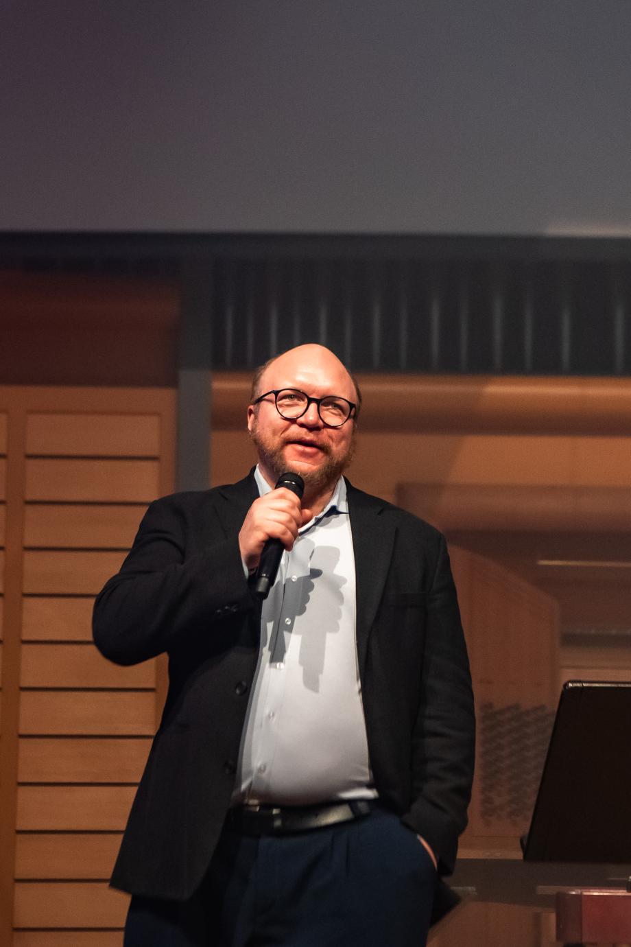 Felix Thiedemann (Leitung Musikvermittlung Internationale Bachakademie) steht mit Mikrofon sprechend auf der Bühne.