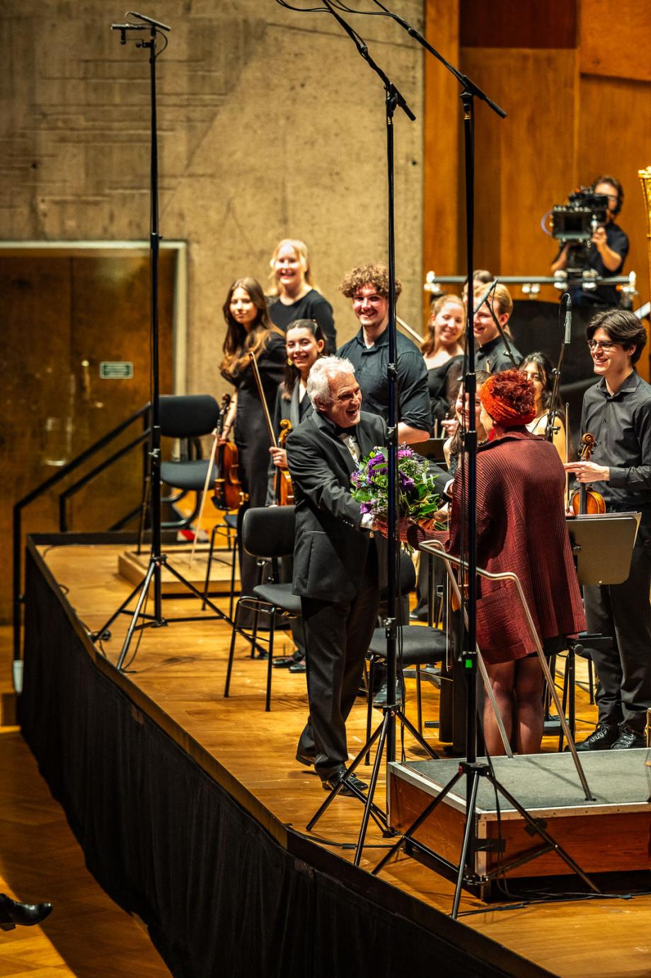 Rektor Axel Köhler überreicht auf dem Konzertpodium einen pinkfarbenen Blumenstrauß an Randi Bubat.