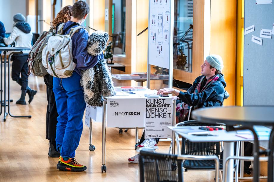 Teilnehmende in der Wandelhalle beim Infotisch im Gespräch.