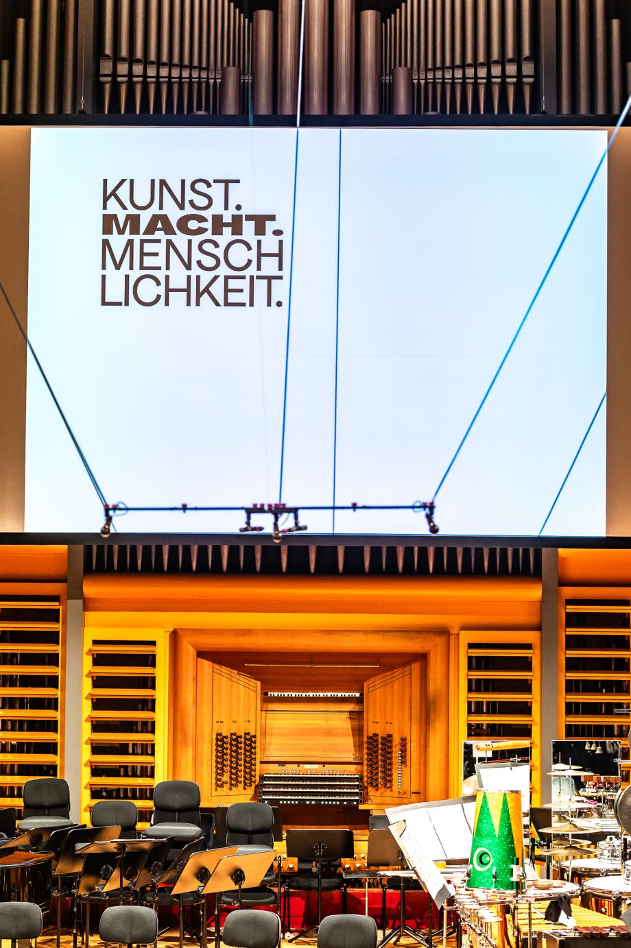Blick auf die Leinwand des Konzertsaal mit dem Titel des Aktionstages: KUNST.MACHT.MENSCHLICHKEIT.