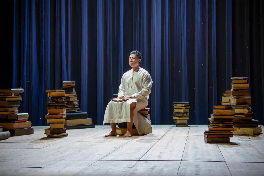 Seneca sitzt im Nachthemd zwischen Bücherstapeln