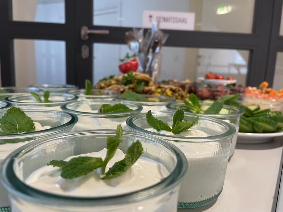 Nahaufnahme des Buffets: Fruchtquark in Gläschen mit einem Minzblatt garniert. Dahinter verschwommen herzhafte Speisen vor einer Tür mit der Aufschrift „Senatssaal“