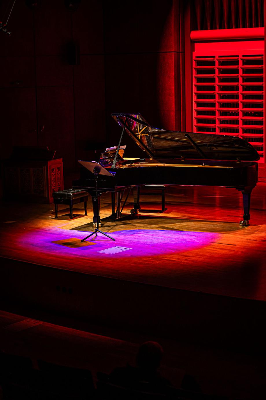 Schwarzer Flügel steht auf Bühne und ist mit rot-pinkem Scheinwerferlicht angestrahlt.
