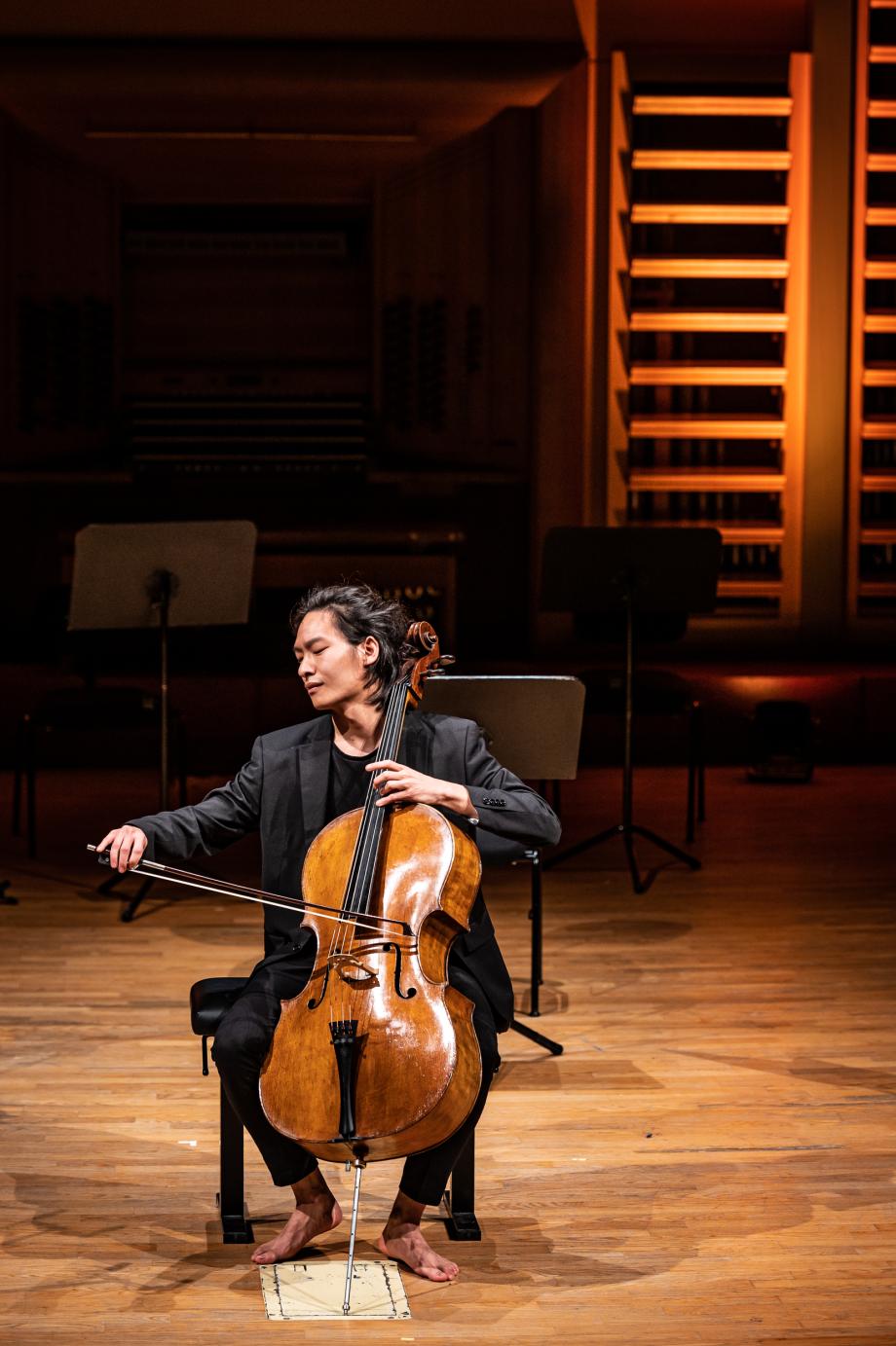Preisträger des Cellowettbewerbs 2022 spielt beim Preisträgerkonzert auf der Bühne des Konzertsaals. Er trägt einen schwarzen Anzug und ist barfuß.